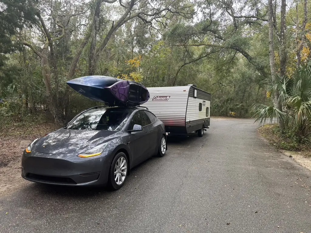 Photo of a Tesla Model Y towing a camper with Kayaks on the roof