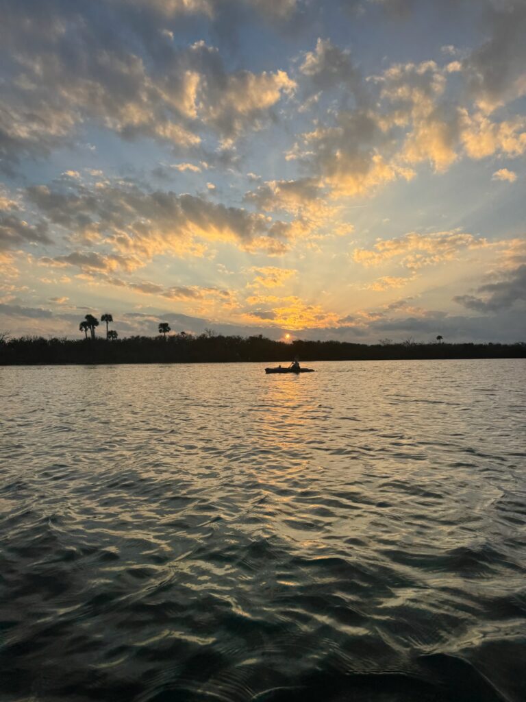 a photo of a kayaker on a large river system, a brilliant sunset in the background