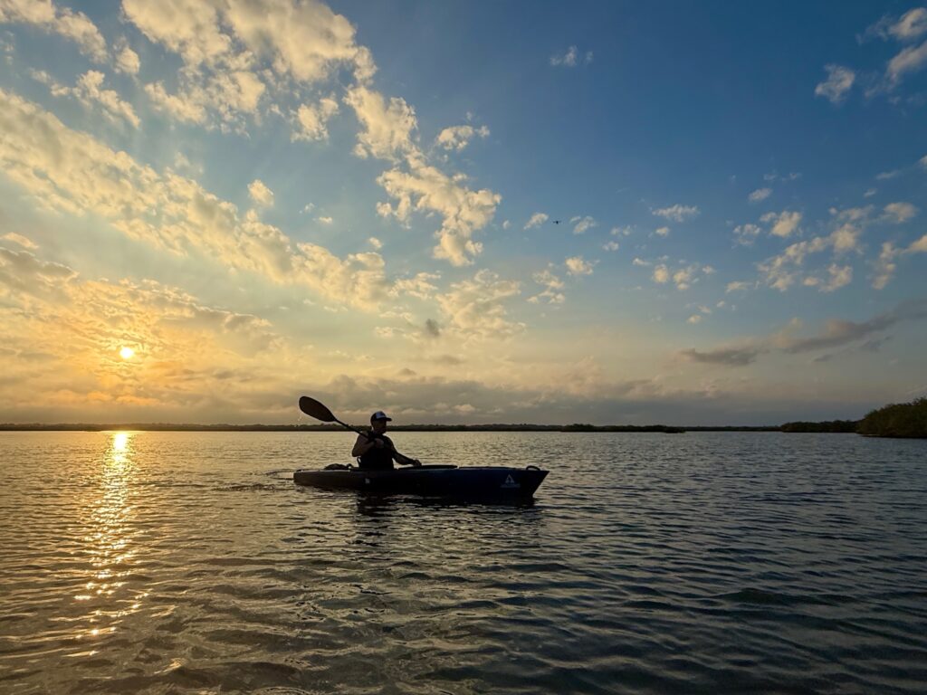 photo of a kayaker in a large river system with a brilliant sunset as the backdrop